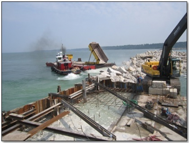 A boat, barge and excavator are building the breakwater.
